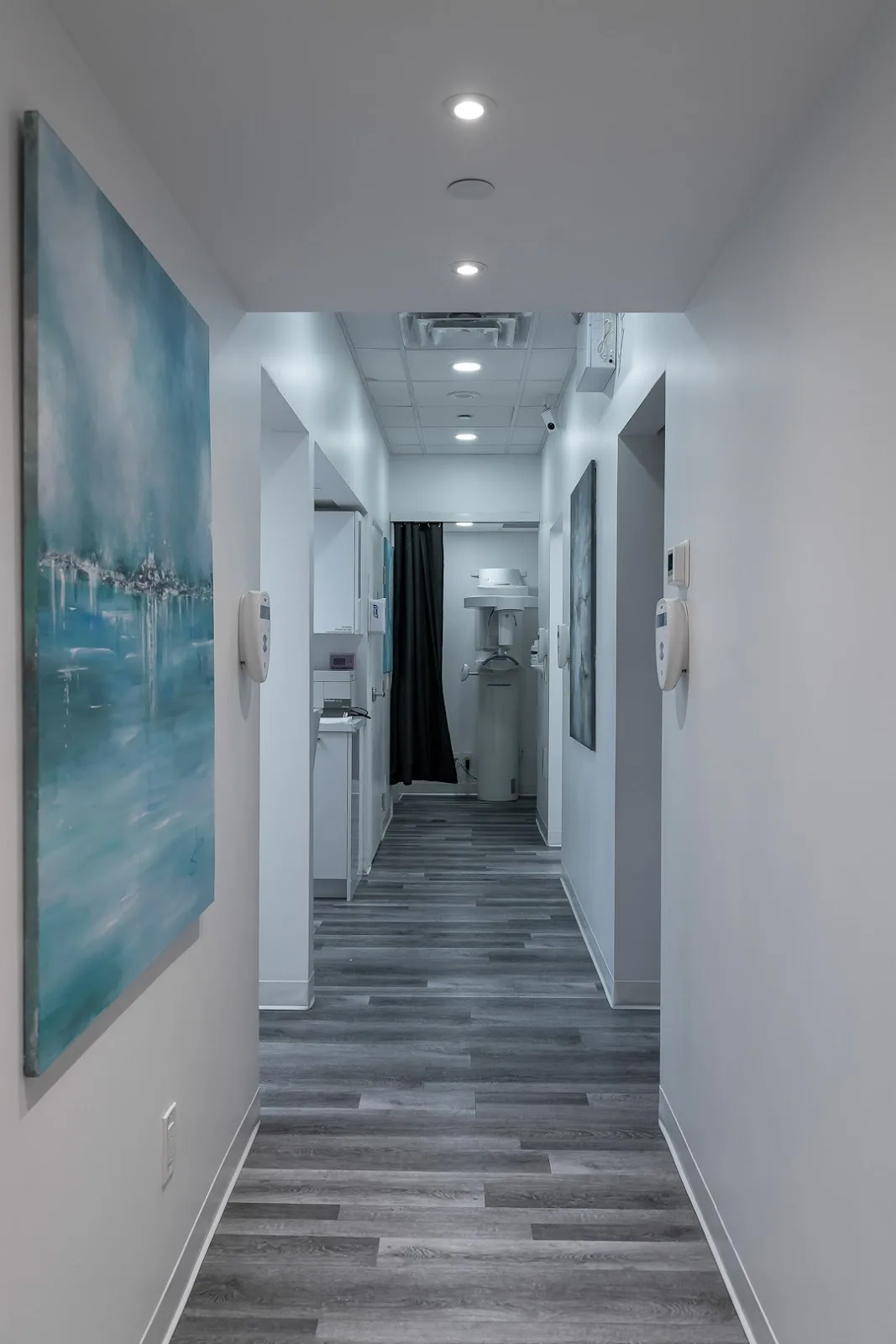 The corridor between the treatment rooms: doorways on both sides, paintings on the walls and the imaging room at the far end